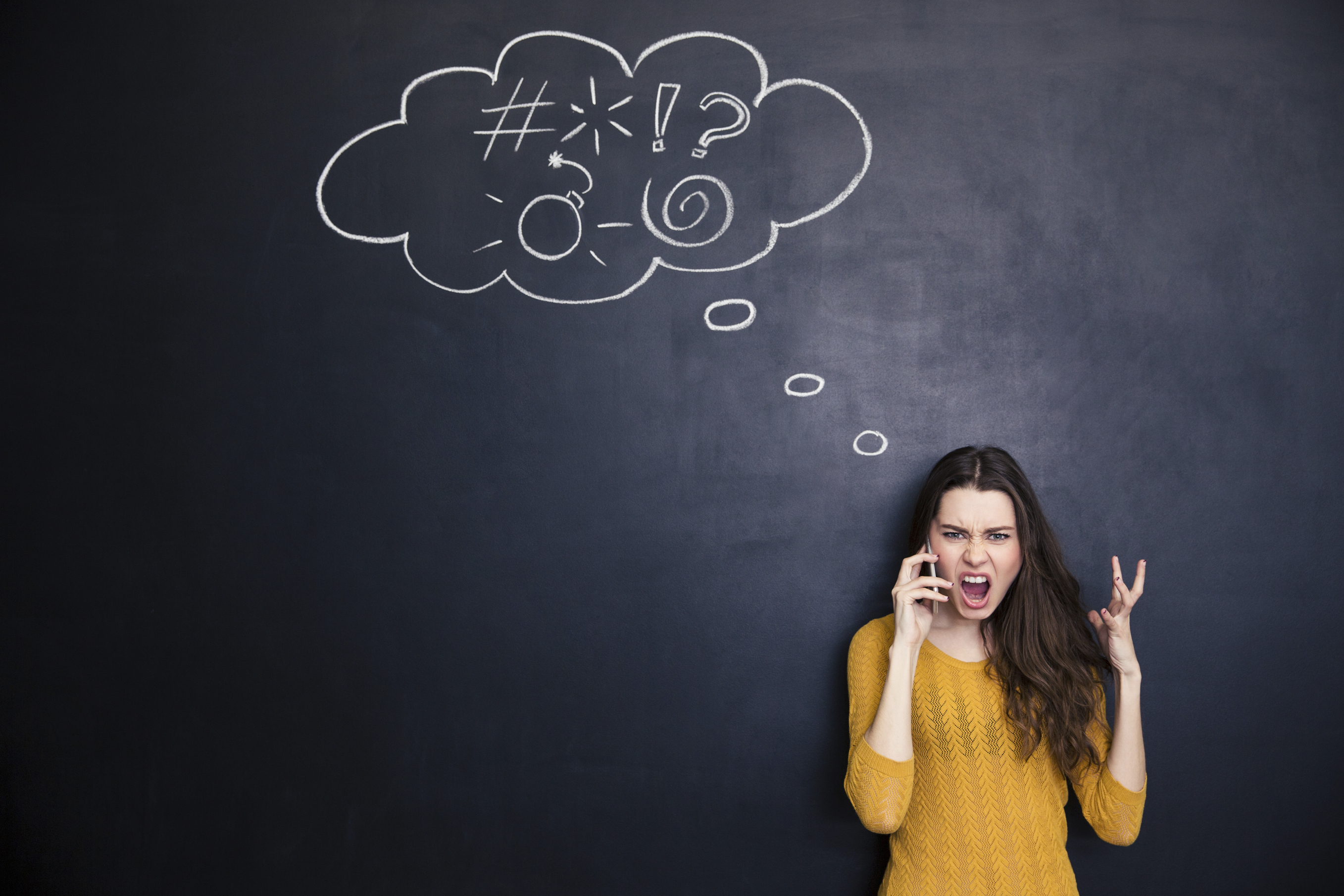 Crazy mad young woman screaming and talking on mobile phone standing over chalkboard backgound